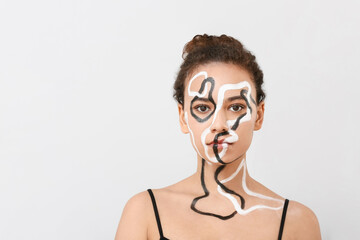 Beautiful young African-American woman with paint on her body against light background