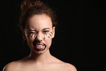 Beautiful young African-American woman with paint on her face against dark background