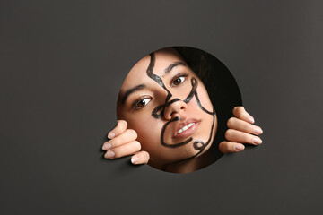 Beautiful young African-American woman with paint on her face visible through hole in dark paper