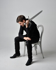 Full length portrait of a  brunette man wearing black shirt and gothic waistcoat holding sword. ...