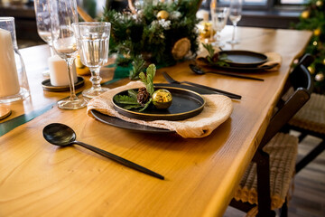 Christmas table setting in rustic style with candles, plates, glasses and eco decors on wooden festive table.New year decorations with fir branches, golden balls, pine cones. Cozy winter holidays.