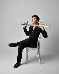 Full length portrait of a  brunette man wearing black shirt and gothic waistcoat holding sword. ...