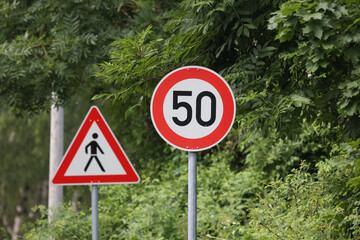 Round speed limit road sign of fifty kilometers per hour with a warning sign of crossing area behind