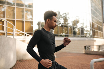 Serious curly brunet dark-skinned man in sport black t-shirt working out. Handsome guy running and looking straight outside.