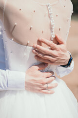 The groom hugs the bride. Vertical photo of the bride and groom. Beautiful buttons on the bride's back. Gentle hugs of the newlyweds