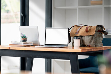 Mockup blank screen laptop with coffee cup and sling bag on wooden table in cafe room.