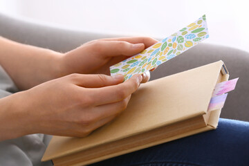 Woman with bookmark and book at home, closeup