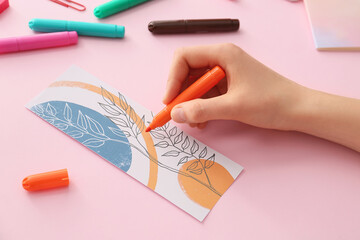 Woman coloring bookmark on color background, closeup
