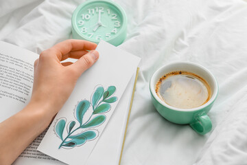 Woman with bookmark and cup of coffee on bed