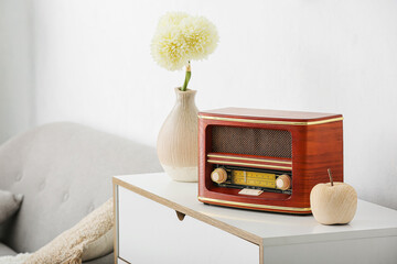 Retro radio receiver and vase with flowers on shelf in room