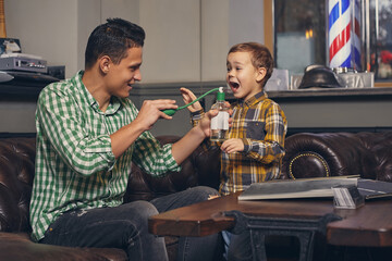 Young father and his stylish little son in the barbershop in the waiting room.