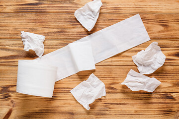 Roll of toilet paper and crumpled sheets on wooden background