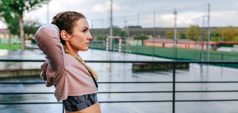 Young sportswoman stretching neck and shoulders outdoors