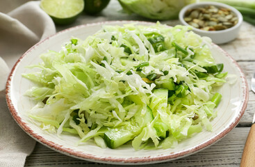 Plate with tasty cabbage salad on light wooden table