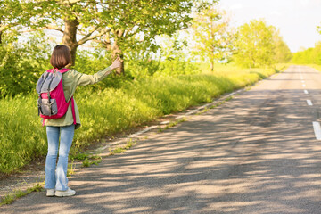 Young woman with backpack hitchhiking on road