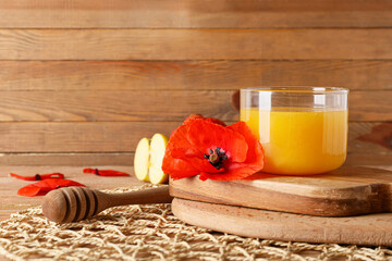 Glass bowl with honey and poppy flower on wooden background