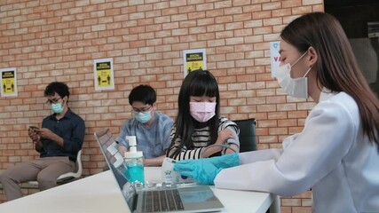 Asian female doctor with face mask checking the girl's health, measuring blood pressure, and use a stethoscope before the virus vaccination people were queuing in the back in the hospital clinic.