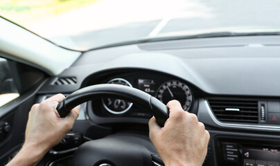 Fototapeta premium Male hands on the steering wheel of a car, inside view. Vehicle management, close-up view of the dashboard and interior. The man behind the wheel.