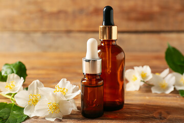 Bottles of essential oil and jasmine flowers on wooden background