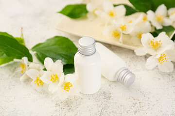 Bottles of cosmetic products and jasmine flowers on light background