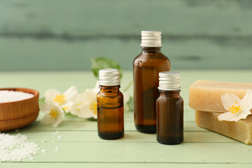 Bottles of essential oil, sea salt, soap and jasmine flowers on color wooden background