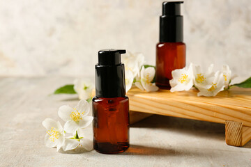 Tray with bottles of essential oil and jasmine flowers on grunge background