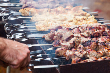 The man's hands are frying a shish kebab on the grill. Pork, chicken and lamb meat on skewers on the grill.