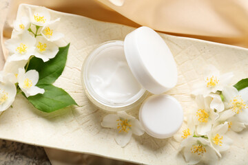 Obraz na płótnie Canvas Plate with jars of cream and jasmine flowers on table, closeup