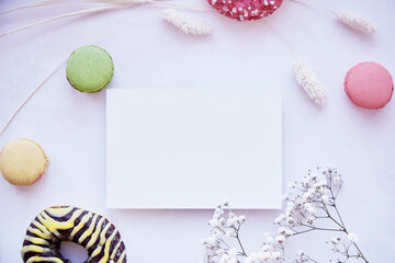 Feminine flat lay. Mock up of stationery card on purple vintage surface. Bright colorful macaroons, donuts and gypsophila. Happy holidays or present card concept. Top view.