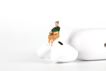 A doll sitting on a Bluetooth earphone and reading a book