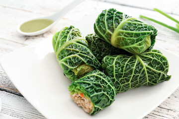 Plate with stuffed cabbage leaves and sauce on light wooden background