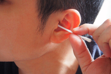 Man using white cotton buds or cotton swabs cleaning his ear canal and earwax at home for...