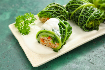 Plate with stuffed cabbage leaves and sour cream on color background