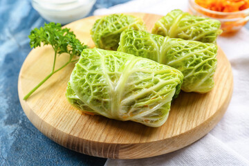 Board with stuffed cabbage leaves on color background