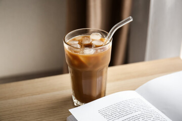 Glass of tasty ice coffee with milk and book on wooden table