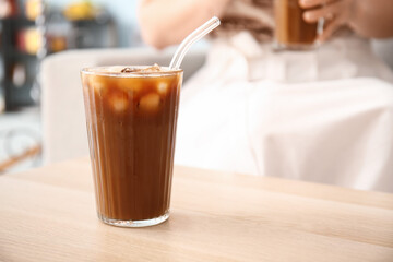 Glass of tasty ice coffee on wooden table in cafe
