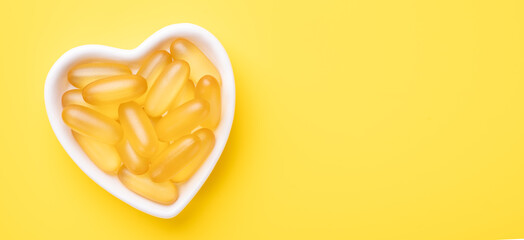 Horizontal banner with Omega 3 capsules in a heart-shaped plate on yellow background. Fish oil softgels. Banner. Copy space