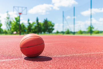 Orange old basketball ball on a red rubber court.Sunny summer warm day.Blurred background.Copy space.