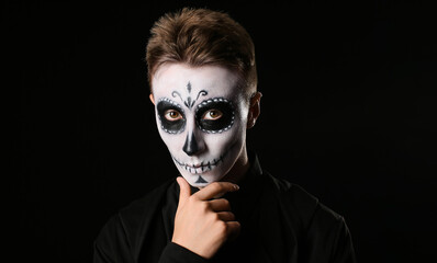 Young man with painted skull on his face for Mexico's Day of the Dead (El Dia de Muertos) against dark background