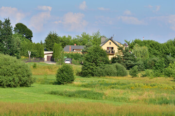 Fototapeta na wymiar View of the estate of detached houses among trees and green meadows. Summer. Day.