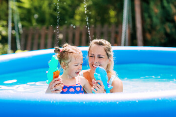 A young mother and her adorable baby are playing in the pool with water pistols, splashing water around