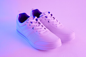 Fashion white sneakers in neon light. Sport shoes for training in the gym. Creative minimalism. 90s concept.