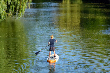 Rear view of man standing and paddling on sup board on green river in summer.