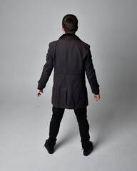 Full length portrait of a brunette man wearing black leather coat.  Standing pose facing backwards,...