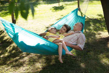 Little child girl with grandparents lie in a hammock in a summer park or garden. Concept of friendly family.
