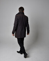 Full length portrait of a brunette man wearing black leather coat.  Standing pose facing backwards,...