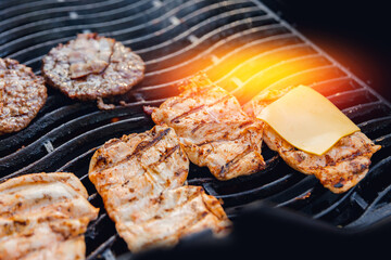 Cook grills burger patties and pork ribs open fire. Turns meat over with tongs
