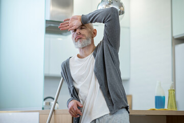 Man in homewear standing with a mop and looking tired