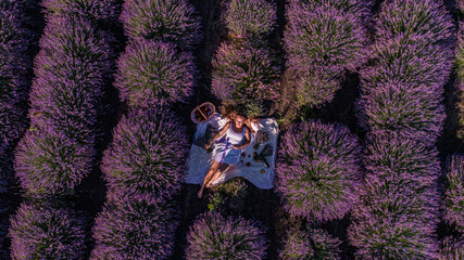 Beautiful girl in white dress on white bedspread in lavender field, shot from drone during sunrise, parallel rows