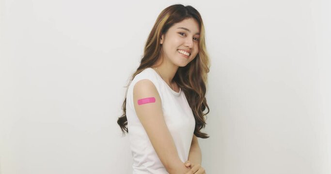 Smiling Asian Woman Shows Bandage On Arm. Happy Asian Woman Feels Good After Received Vaccine On White Background.